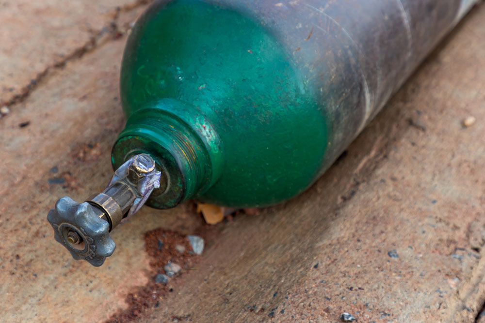 Aging green gas cylinder tank awaiting torch and regulator repair